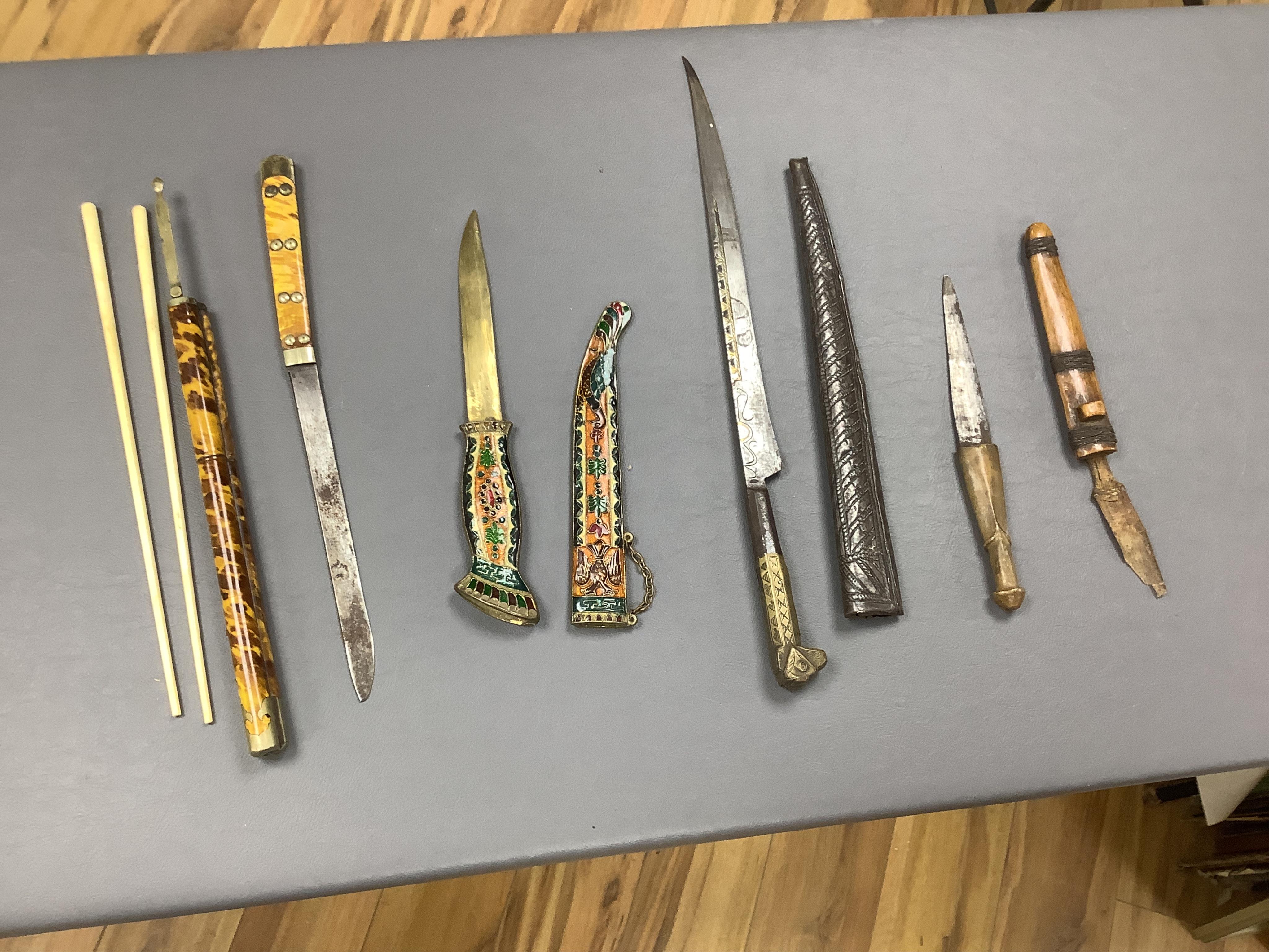 Eighteen assorted world weapons comprising a silver jambya (pommel missing), a knobkerry, a dha, two kris (one with handle missing), a lohar, three kukris, a djambok, a Chinese trousse, a chora, a flyssa, five others and